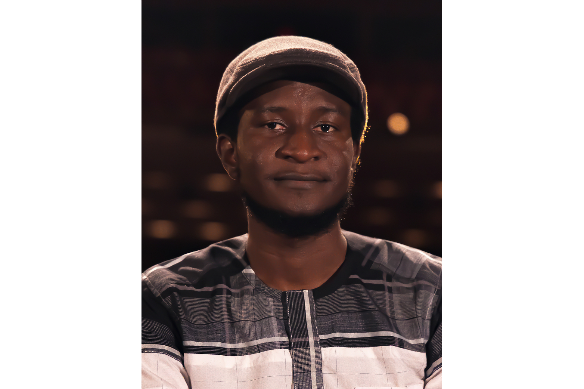 Poet Saddiq Dzukogi in a newsboy cap and plaid shirt with a dark starry background